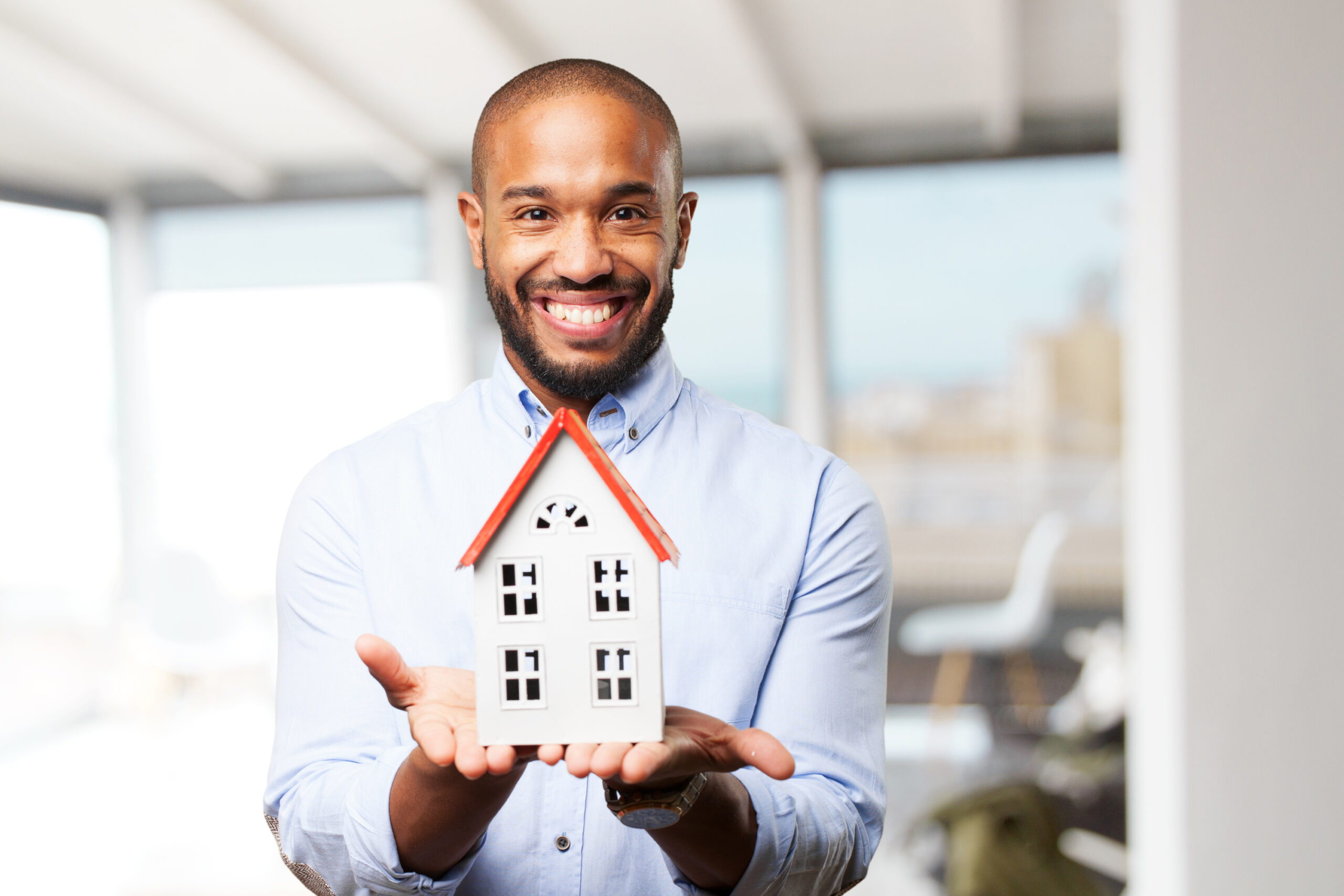 Person in a light blue shirt holding a small model house